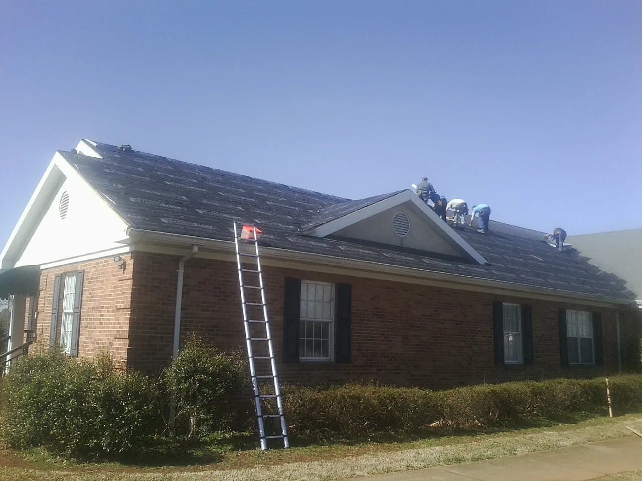 Crew tearing shingles off a brick ranch roof with a ladder set — Emergency Roof Repair work by our crew in Currie