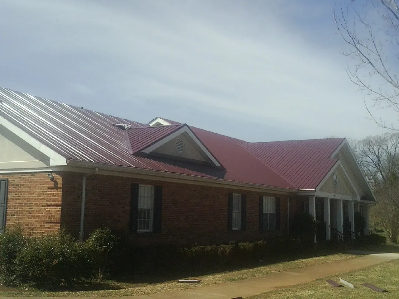 Red metal roof with gabled entries on a long brick building, from a Hail Damage Roof Repair job in Currie
