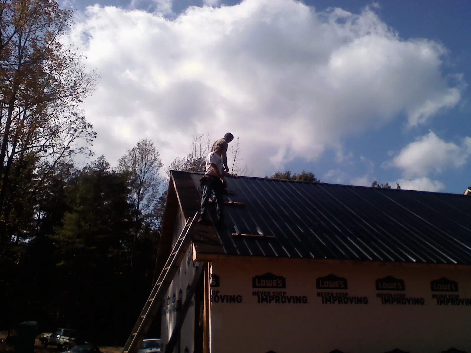 Roofer fastening dark metal panels high against a cloudy sky, from a Roof Inspection job in Currie