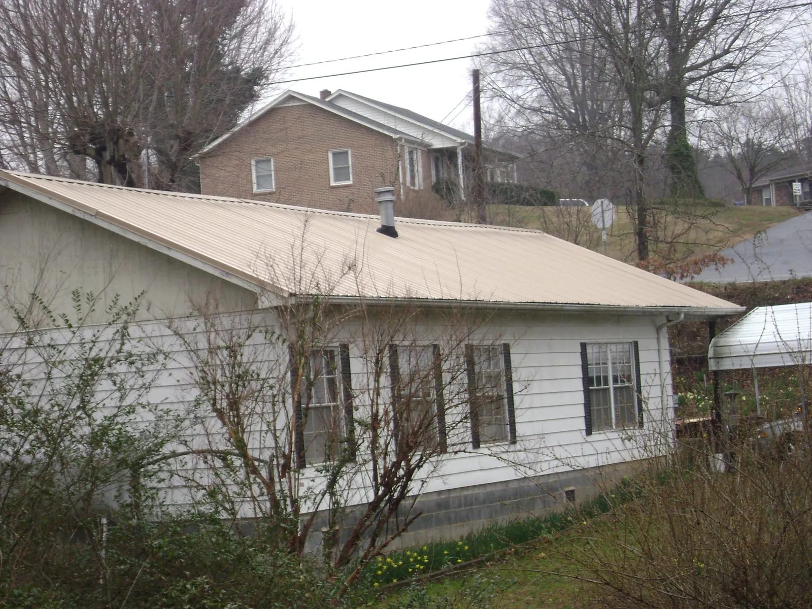 Tan metal roof on a white sided house set into a hillside — Commercial Roofing by Roofing Brothers in Currie